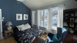 Una camera da letto con un letto, una sedia, una lampada, una libreria e una finestra vista alberi innevati.