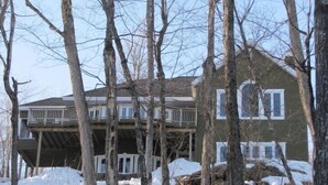 Una casa a due piani con un balcone, immersa tra alberi e neve.