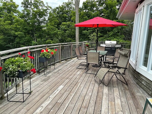 A wooden deck with a table and chairs, a red umbrella, and planters with red flowers.