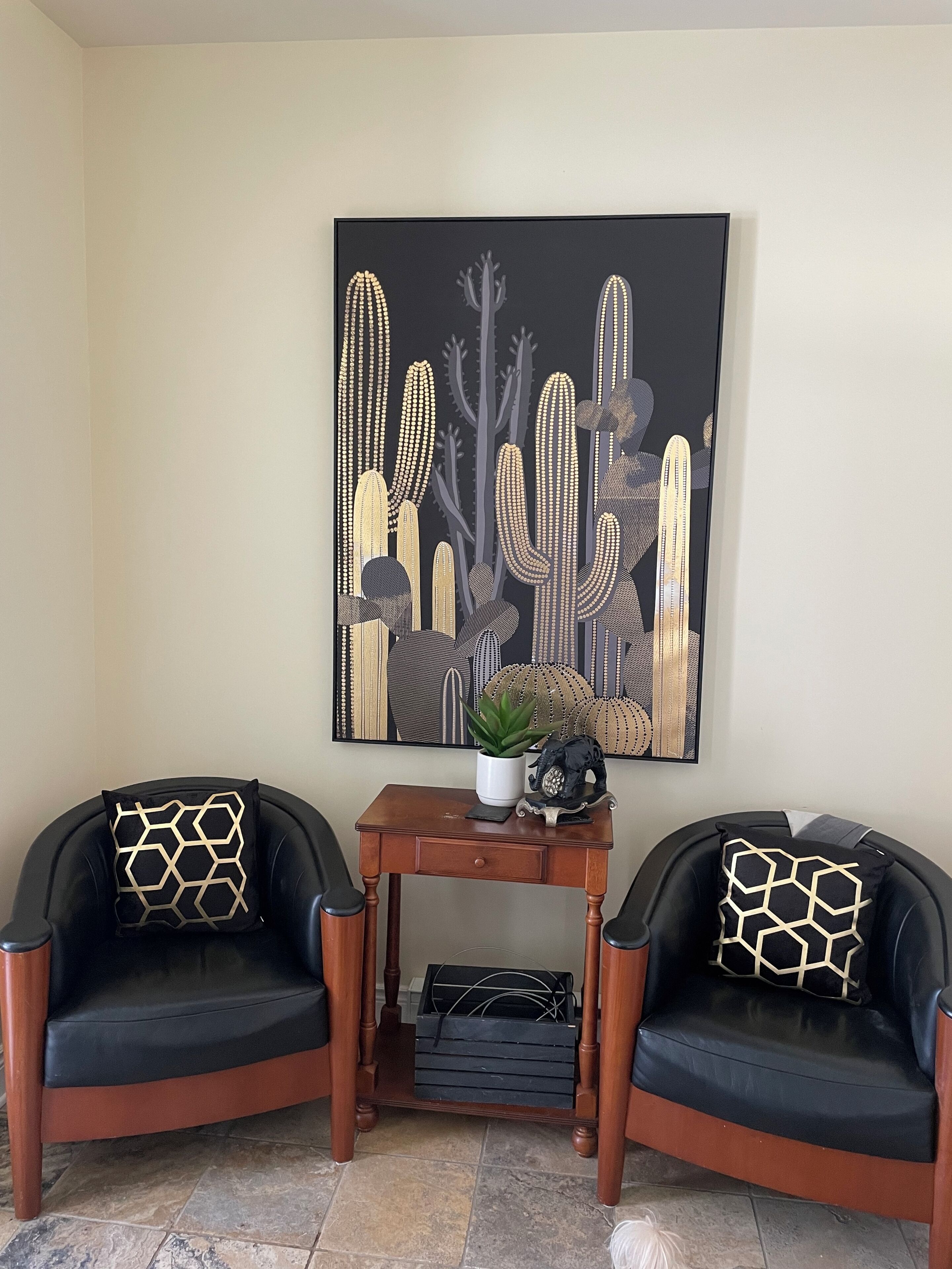 A room with two black leather chairs, a wooden table with a potted plant, and a large black and gold artwork on the wall.