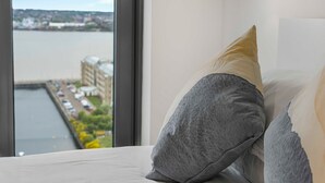 Une chambre d’hôtel dotée d’une grande fenêtre donnant sur une rivière et les bâtiments situés de l’autre côté.