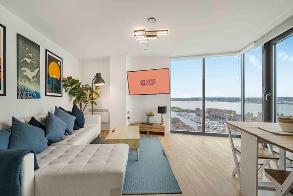 Ein modernes Wohnzimmer mit einer Couch, einem Couchtisch und einem Fernseher, der „GUEST READY“ anzeigt.