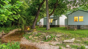 Ein rustikales Blockhaus mit einem kleinen Bach, umgeben von üppigem Grün und Bäumen.