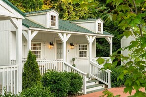 Een wit houten huis met een groen dak, een veranda met witte leuningen en een trap naar de ingang.