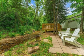 A wooden deck with Adirondack chairs, a small wooden table, and a metal barrel.