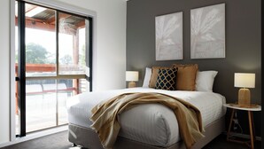 A bedroom with a large bed, two wall-mounted lamps, and a sliding glass door leading to an outdoor area. - Family Comfort in the Stunning Sisters Beach (Sisters Beach)