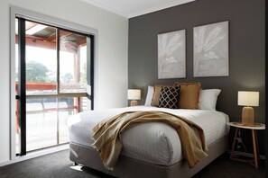 Un dormitorio con una cama grande, dos lámparas fijadas a la pared y un ventanal corredero que da a un área exterior.