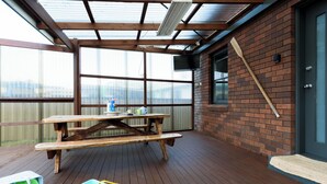 A wooden deck with a picnic table, a brick wall, and a door. - Family Comfort in the Stunning Sisters Beach (Sisters Beach)