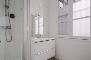 A bathroom with a glass shower enclosure, a white sink, and a mirror above it.
