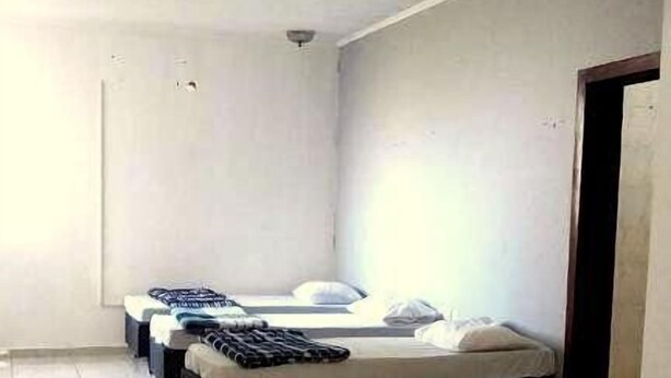 Habitación de hotel con tres camas dispuestas en fila, piso de baldosas y pared blanca lisa.