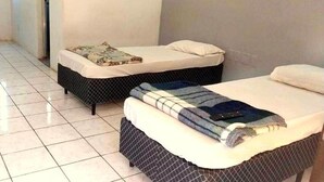 Dos camas individuales con ropa de cama estampada, suelo de baldosas y pared lisa.
