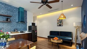A modern kitchen with a blue backsplash, a dining area with a wooden table and chairs, a blue sofa, and a ceiling fan.