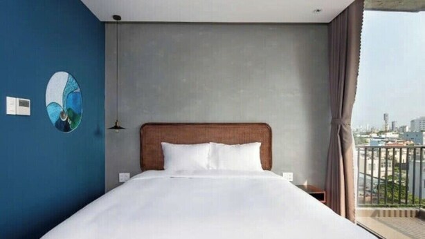 A hotel room with a large bed, a view of the city through the window, and a blue accent wall.