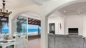 A spacious living area with a grey sofa, a dining table with chairs, and a view of the beach.