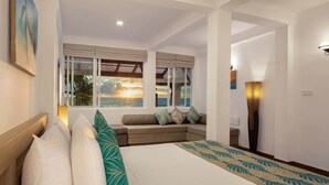 A bedroom with a bed, a sofa, a large window with a view of the sea, and a nightstand with a lamp.