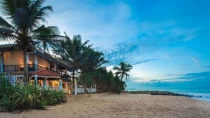 A beachfront property with a two-story building, a balcony, and palm trees.