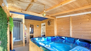 A wooden cabin with a hot tub, wooden walls, and a ceiling with exposed beams.