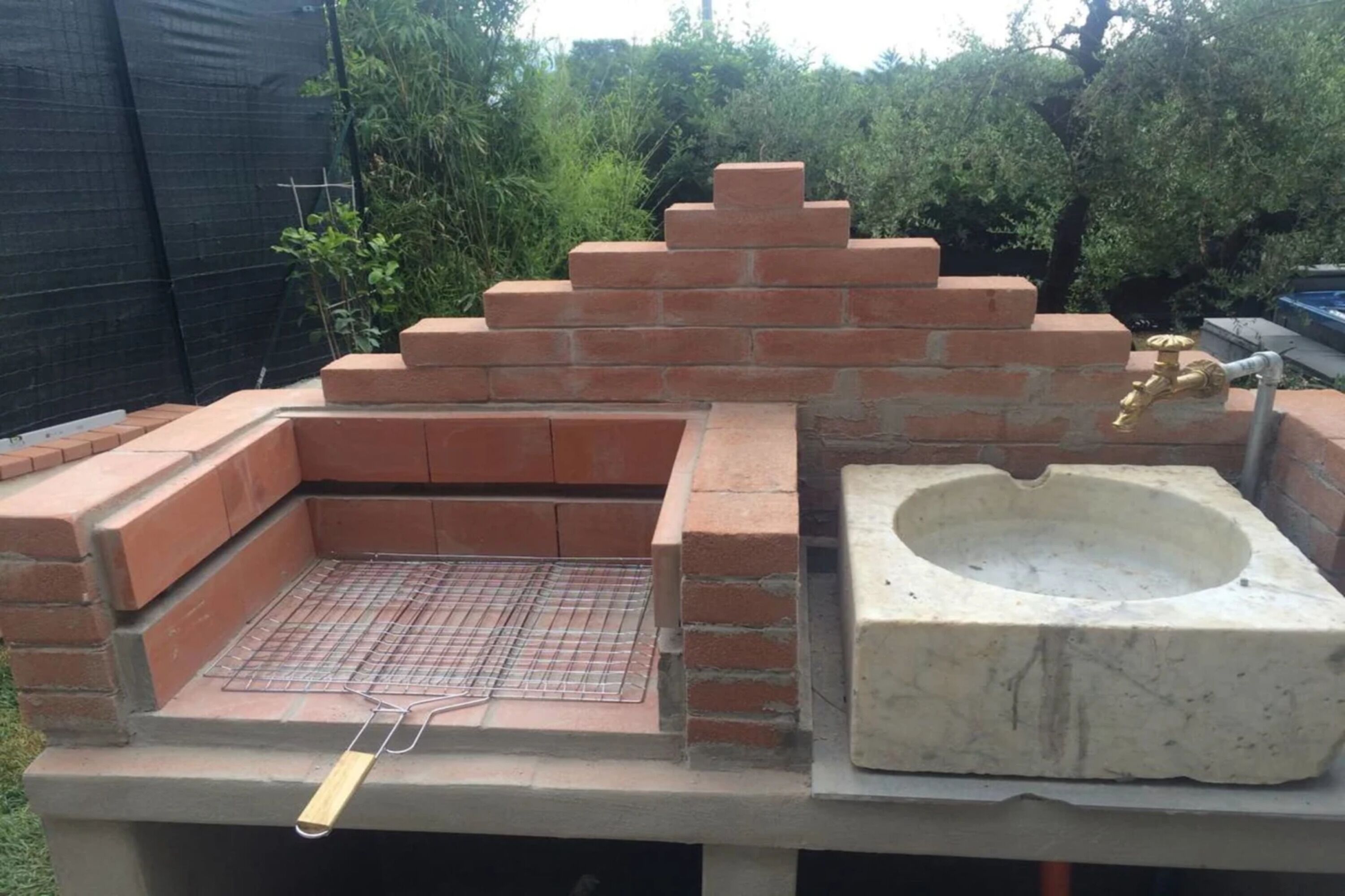 An outdoor barbecue area with a brick oven, a grill, and a stone sink.