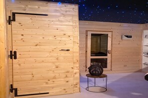Una habitación de madera con techo estrellado, una puerta, una ventana y una mesita con un florero.