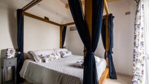 A bedroom with a four-poster bed, a nightstand, and a window with floral curtains.