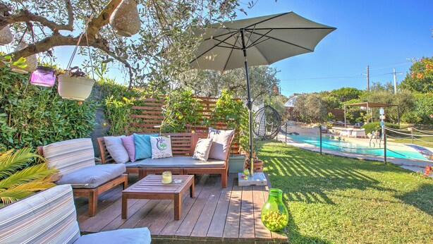 A wooden deck with outdoor furniture, a pool, and a pergola with hanging lights.