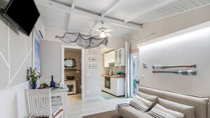 A living room with a sofa, a TV, and a ceiling fan. There is a kitchen in the background.