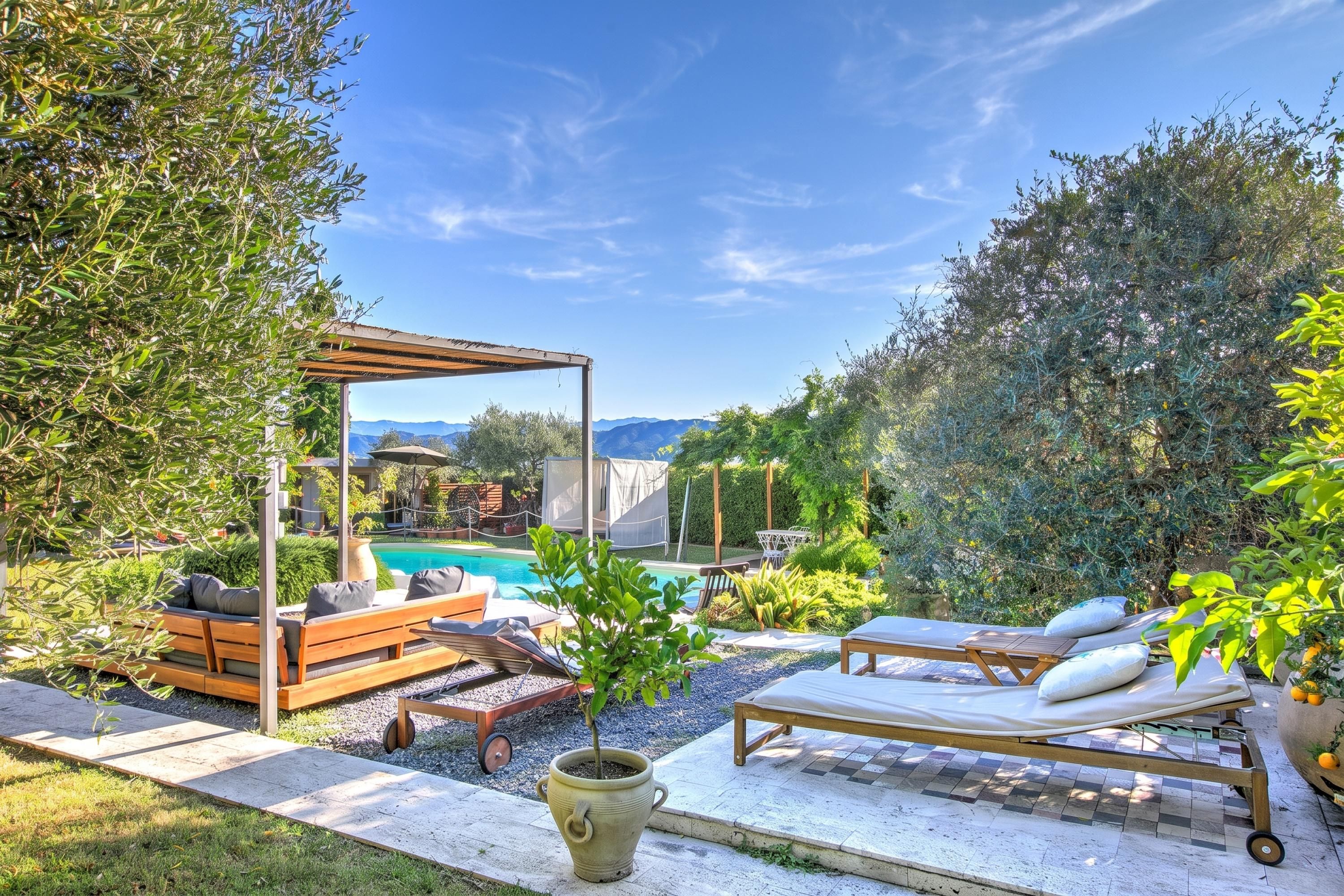 A poolside area with lounge chairs, a pergola, and a view of mountains in the background.