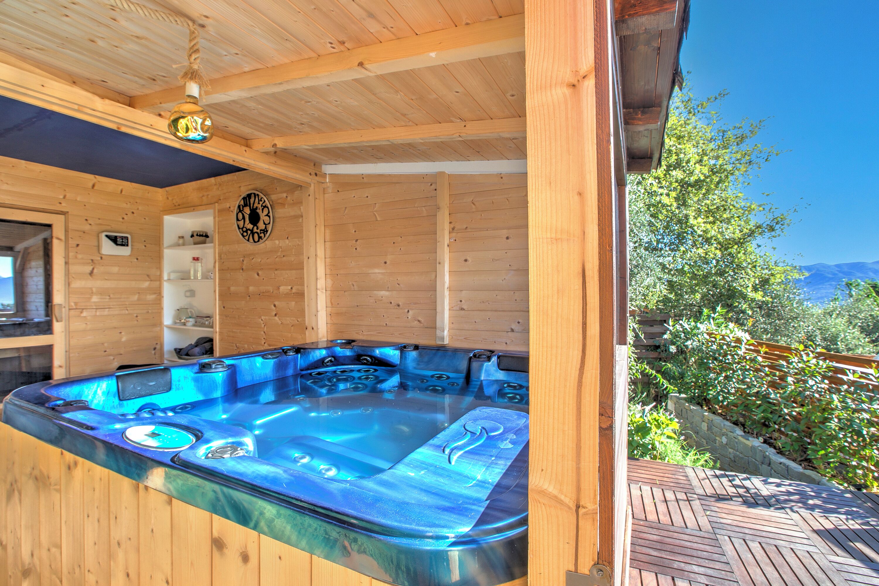 A wooden spa area with a hot tub, wooden walls, and a view of greenery and mountains.