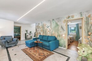 A living room with a blue sofa, a patterned rug, a green dinosaur toy, and a mural with floral and cactus designs. - Casa Fra Gli Ulivi - Ponente, Ameglia, Italy (Ameglia)