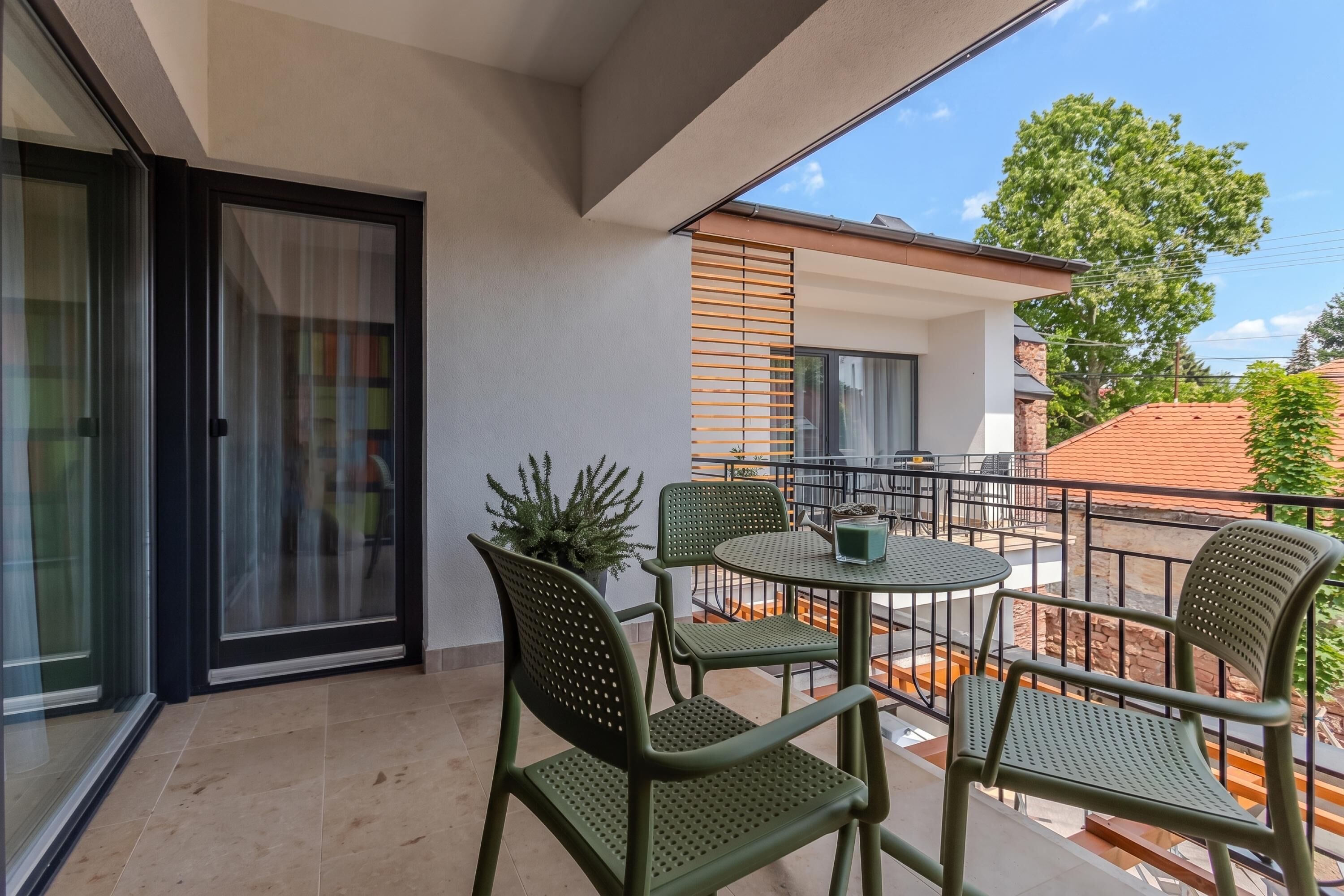 Een balkon met een tafel, stoelen, een bloempot en uitzicht op een gebouw met een pannendak.