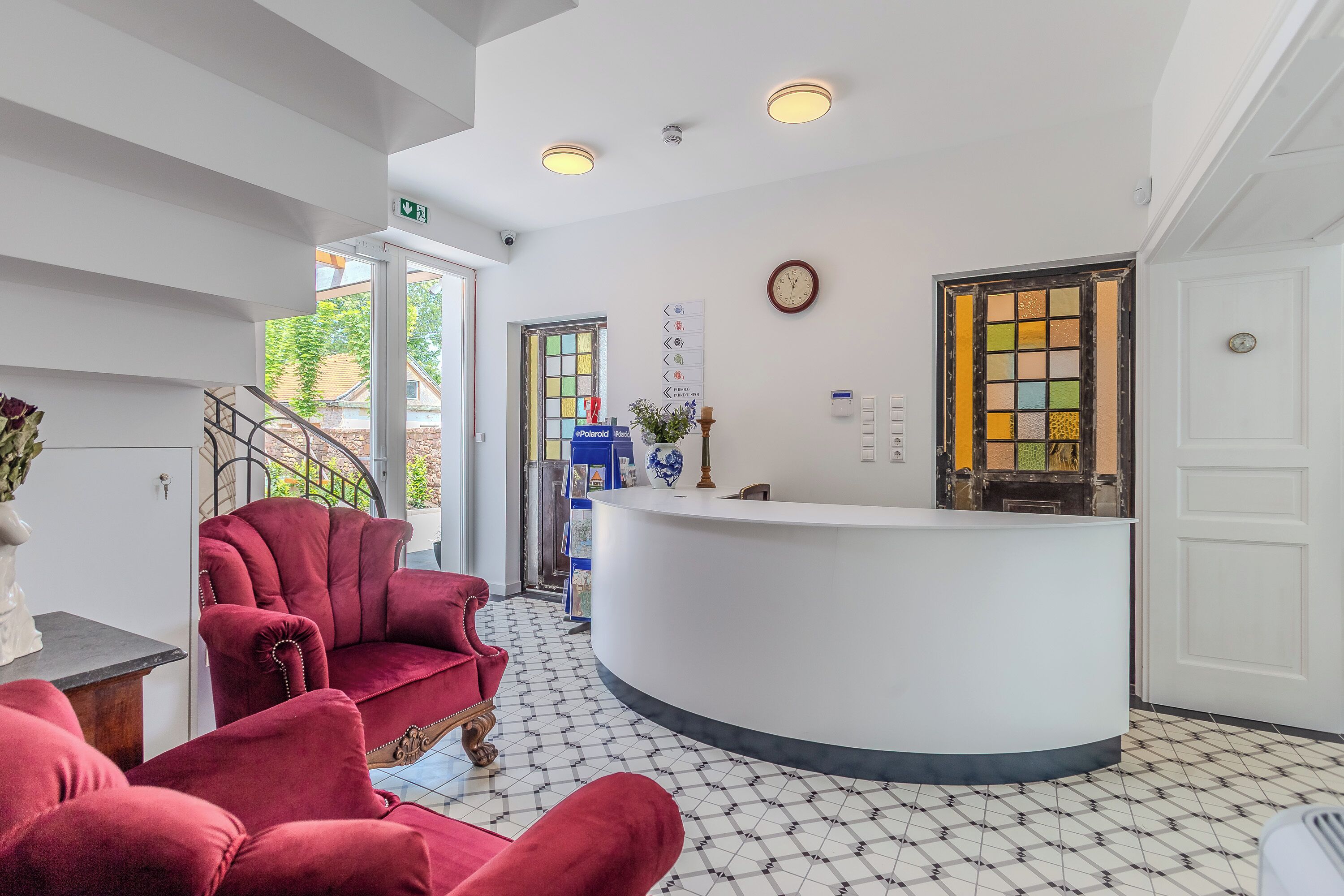 A reception area with a white reception desk, red velvet chairs, a staircase, and a tiled floor.