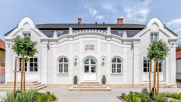 A white building with a central entrance, arched windows, and a sign above the door.