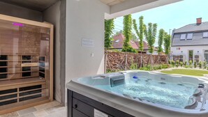 A hot tub with a stone wall and wooden deck in a backyard.
