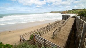 A wooden boardwalk leading to a beach with a view of the ocean and cliffs.