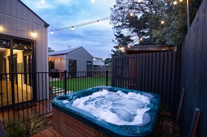 A hot tub in a backyard with a wooden fence, string lights, and a house in the background.