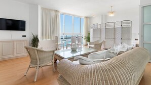 Una sala de estar moderna con una mesa de centro de vidrio, muebles de mimbre, un televisor de pantalla plana y vistas al mar.