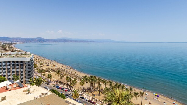 Un hotel frente al mar con vista a la playa, varios pisos y una zona de estacionamiento.