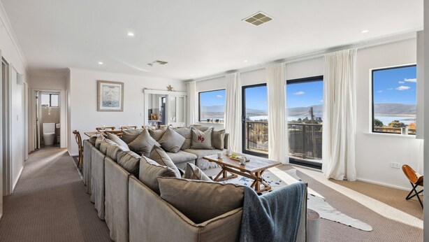 A spacious living room with a large sectional sofa, a dining area, and large windows offering a scenic view. - Avalon: a striking five-bedroom, three-bathroom holiday rental. (Jindabyne)