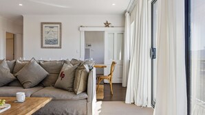 A modern living room with a sofa, a wooden coffee table, and a dining area with a chair and table. - Avalon: a striking five-bedroom, three-bathroom holiday rental. (Jindabyne)