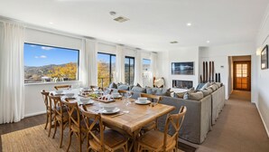 A spacious dining area with a wooden table and chairs, a sofa, and a fireplace. - Avalon: a striking five-bedroom, three-bathroom holiday rental. (Jindabyne)