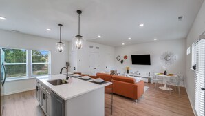 A modern kitchen with a central island, a dining area with a round table, and an orange sofa. - New Stylish Townhome in Cotswold with Ensuite Baths, Chef's Kitchen & EV Charger (Charlotte)