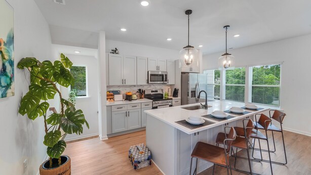 A modern kitchen with white cabinetry, a central island with bar stools, and a large window providing natural light. - New Stylish Townhome in Cotswold with Ensuite Baths, Chef's Kitchen & EV Charger (Charlotte)