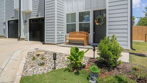 A residential building with two garages, a front porch with a bench, and a small garden area with a decorative frog statue. - New Stylish Townhome in Cotswold with Ensuite Baths, Chef's Kitchen & EV Charger (Charlotte)