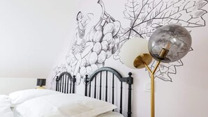 A bed with white bedding, a black metal headboard, and a wall mural of grapes and leaves.