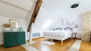 A bedroom with a sloped ceiling, a bed, a green dresser, a white rug, and a brick wall.