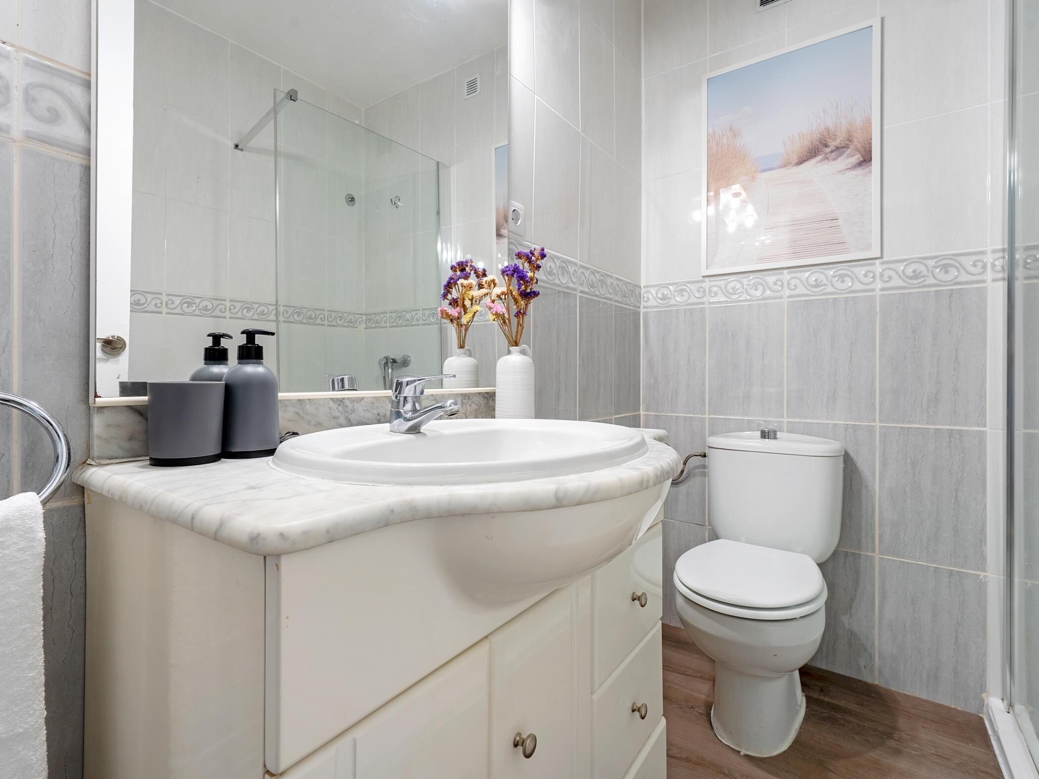 A bathroom with a white sink, a toilet, and a shower. There are two bottles of shampoo and conditioner on the counter.