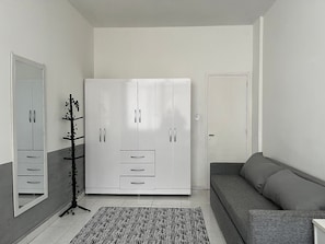 Una habitación con un armario blanco grande, un sofá gris y un tapete blanco y negro.