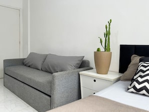 Un dormitorio moderno con un sofá gris, un cactus grande en maceta y una cama con cabecera negra.