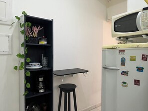 A kitchen with a refrigerator, microwave, and a black shelf unit with kitchen utensils. - Studio em Copacabana perto da praia (Rio de Janeiro)
