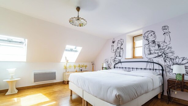 A bedroom with a large bed, wooden flooring, a ceiling fan, and a mural on the wall. - Logis Marie (flavigny sur Ozerain)